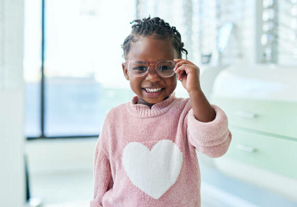 Young girl with glasses smiling at the camera in a heart sweater.