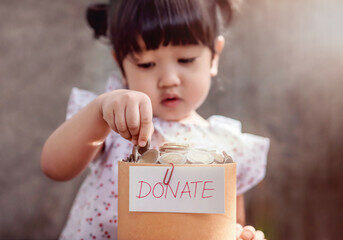 Young girl placing a coin into a donation box.